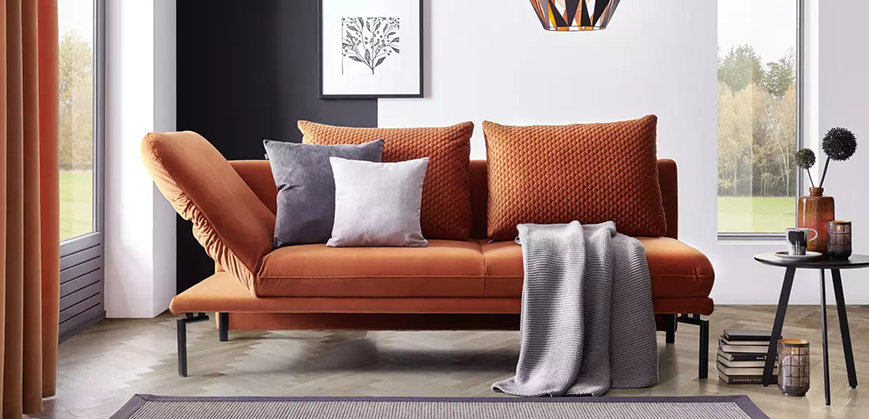 Orange Polsterliege mit aufgeklappter Sitzfläche, Dekokissen und Decke