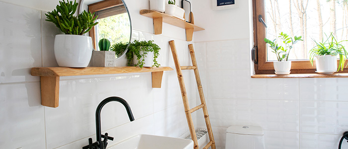Inneneinrichtung eines kleinen Badezimmers mit Holzregal und Holzleiter, modernem Waschbecken und rundem Spiegel an einer weißen Wand